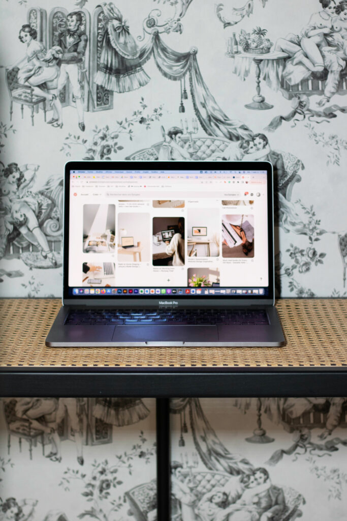 Ordinateur portable affichant un moodboard MNDS sur une console en cannage, devant un papier peint toile de Jouy